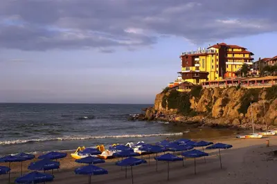 a group of blue umbrellas on a beach with a building at Hotel Parnasse in Sozopol