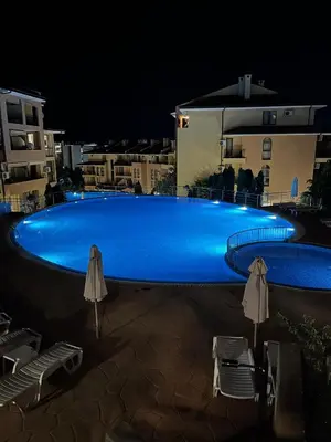 a blue swimming pool at night with chairs and umbrellas at Paradise Dreams Studio in Sveti Vlas