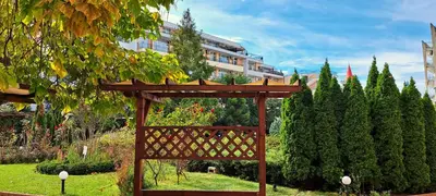 a wooden structure in a garden with trees and a building at Apartament Amelia in Sunny Beach