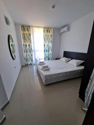 a bedroom with a white bed and a window at Апартамент БАНГЕВИ in Burgas City