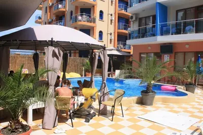 a woman sitting in a chair under an umbrella next to a swimming pool at Mirage Family Hotel in Primorsko
