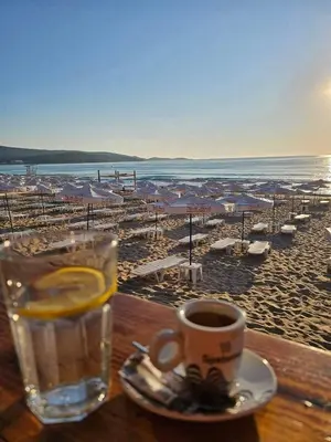 a cup of coffee and a glass of water on the beach at Family Hotel Magnolia - Summer residence in Primorsko