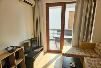 a living room with a couch and a television and a balcony at Двустаен апартамент Поморие in Pomorie