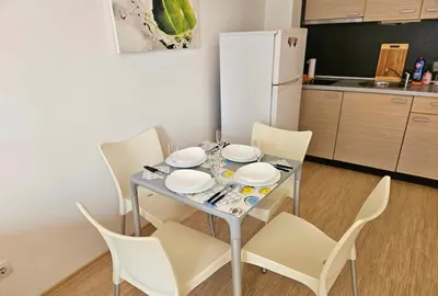 a dining room table with white chairs and a white refrigerator at Двустаен апартамент Поморие in Pomorie