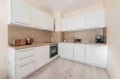 a white kitchen with white cabinets and a wooden floor at Varna Beach Apartment in Varna City