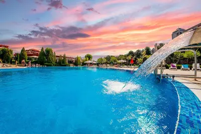 a fountain in a pool with a sunset in the background at Orchid Fort Noks Design in Sunny Beach