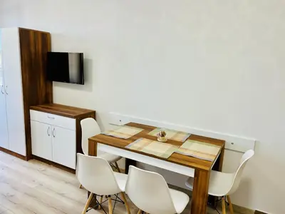 a dining room table with white chairs and a television at Апартаменти Тутхон Поморие in Pomorie