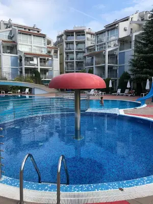 a swimming pool with a red umbrella in front of some buildings at Elit 2 Apartment in Sunny Beach