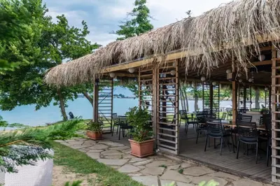 a restaurant with a thatched roof and tables and chairs at Marina Trio in Sozopol