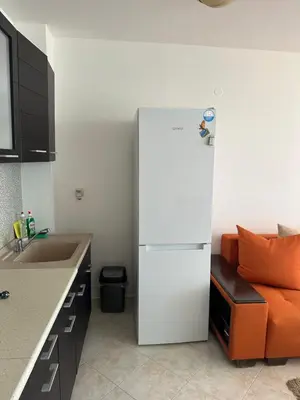 a white refrigerator in a kitchen with an orange couch at Apartament Sunset Kosharitsa - Slunchev briag in Kosharitsa