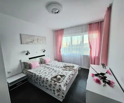 a bedroom with a bed and a window with pink curtains at Rose Garden Deluxe in Chernomorets