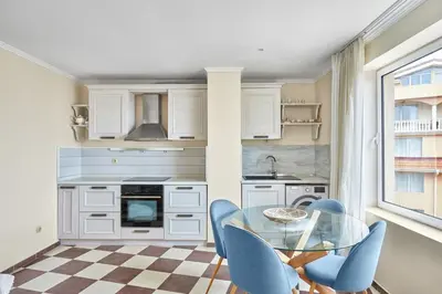 a kitchen with a glass table and blue chairs at Beach Front Luxury Apartment in Sozopol