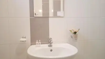 a white bathroom with a sink and a mirror at Апартамент в непосредствена близост до плажа in Burgas City