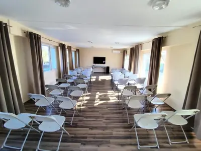 a room with rows of white chairs and a table at Хостел Спортна база Ветрен in Burgas City