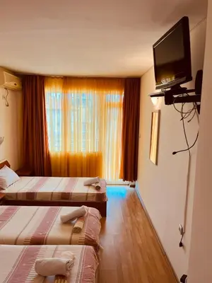 a hotel room with two beds and a flat screen tv at Хотел Стоянови in Ravda