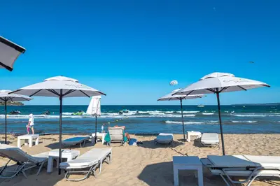 a beach with chairs and umbrellas and the ocean at Апартаменти с чадъри и шезлонги на плажа - Свети Никола Каваците in Sozopol