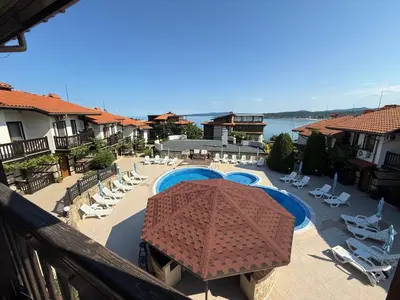 a balcony of a resort with a pool and chairs and an umbrella at Cosy Seaview apartment Budjaka in Sozopol