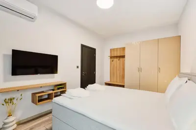 a white bedroom with a bed and a tv at Marina Bay Apartments Kraymorie in Burgas City