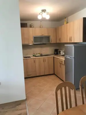 a kitchen with wooden cabinets and a stainless steel refrigerator at Тристаен апартамент в затворен комплекс in Chernomorets