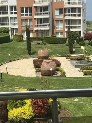 a park with a bench and flowers in front of a building at Тристаен апартамент в затворен комплекс in Chernomorets