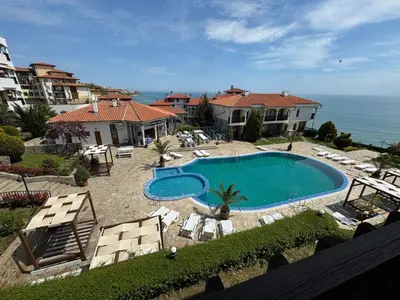 a swimming pool with chairs and a house and the ocean at Sun Coast by the Sea in Sveti Vlas