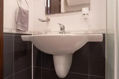 a white sink in a bathroom with black tiles at Делукс Апартамент Лазур Поморие in Pomorie