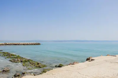 a beach with blue water and a rocky shore at Marea 2 in Pomorie