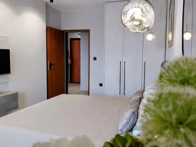 a bedroom with a large white bed and a chandelier at Ika Apartment Central in Burgas City