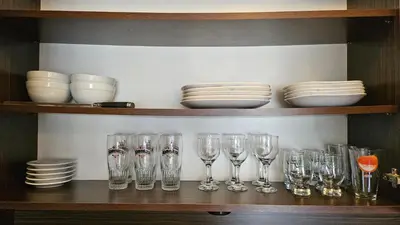 a shelf with wine glasses and plates and bowls at Апартамент Комфорт in Varna City
