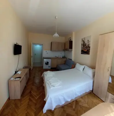 a bedroom with a white bed and a kitchen at Студио Слънчева перла in Burgas City