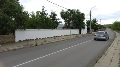 a car is driving down a road with a white wall at Къща за гости Veranda Raia Поморие in Kamenar
