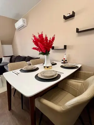 a dining room table with a vase of red flowers on it at Urban Nest Varna - Near Center and Bus Station in Varna City