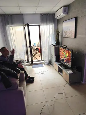 a man sitting on a couch watching tv in a living room at Tarsis nova slunchev Briak Apartament 08 A in Sunny Beach
