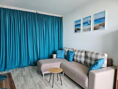 a living room with a couch and blue curtains at 2BR Sea Sunrise View Apartment Happy Place in Chernomorets