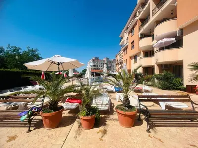 a resort with chairs and an umbrella and palm trees at Kasandra Apart Hotel in Sunny Beach
