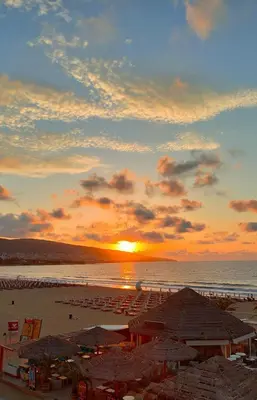 a sunset over a beach with umbrellas and the ocean at Sunny Bay Sweet Homes Lux Apartment in Sunny Beach