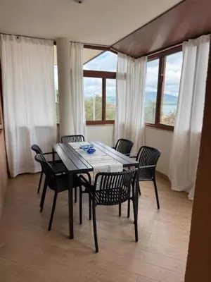 a dining table and chairs in a room with windows at Апартамент Созополски Залез in Sozopol