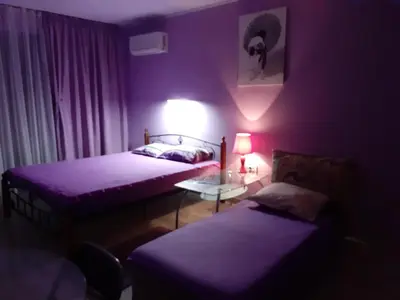 a purple room with two beds and a table with a lamp at Parus 4 Studio in Pomorie