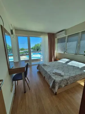 a bedroom with a bed and a desk and windows at Първа Линия Лазур Поморие in Pomorie
