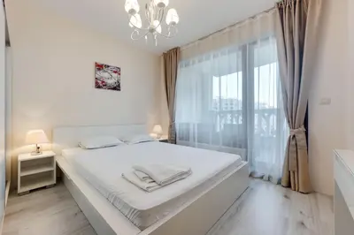a white bedroom with a large bed and a window at АТ apartment - South Bay Beach Residence in Varna City