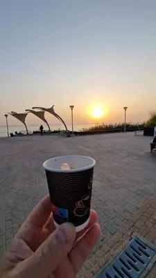 a hand holding a coffee cup with the sunset in the background at Family Hotel California in Primorsko