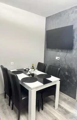 a white table with black chairs and a tv on a wall at Апартамент Велкови in Tsarevo