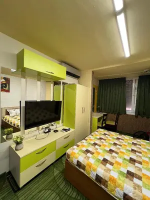 a bedroom with a bed and a desk with a television at Апартамент Боги in Burgas City