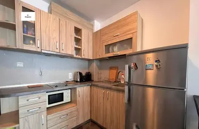 a kitchen with wooden cabinets and a stainless steel refrigerator at Двустаен апартамент с морска панорама в Blue Bay Palace in Pomorie