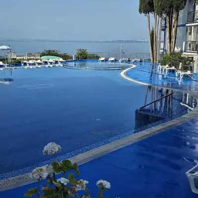 a large swimming pool with blue water and chairs at Двустаен апартамент с морска панорама в Blue Bay Palace in Pomorie