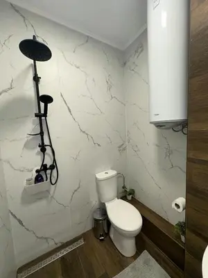a bathroom with a toilet and a white marble wall at Апартамент за нощувки и отдих in Burgas City