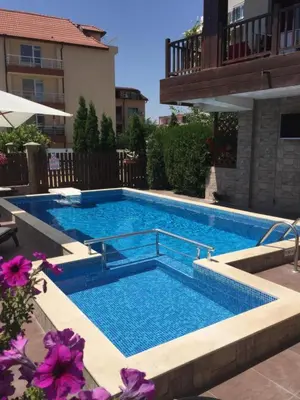 a large swimming pool in a yard with purple flowers at The White Houses 7 in Nesebar