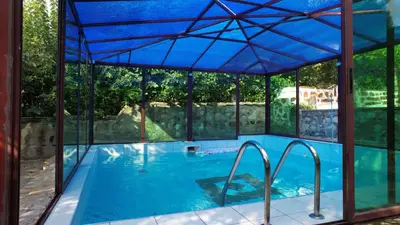an indoor swimming pool with a blue roof and glass walls at Вила Лонгоз