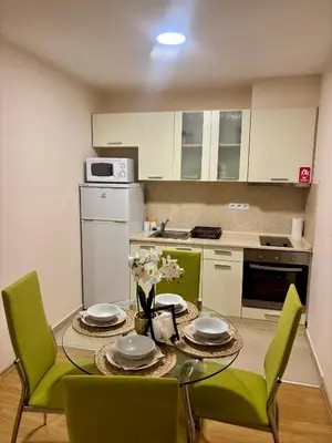 a kitchen with a table with green chairs and a kitchen with white cabinets at Luxury Premier Fort Beach in Sveti Vlas