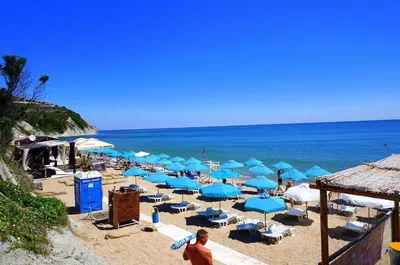 a beach with blue umbrellas and chairs and the ocean at Апартаменти Бяла Клиф - Byala Cliff Apartments in Byala